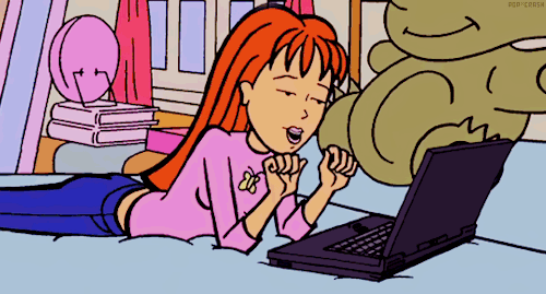 Animated cartoon of a girl with orange hair lying on her bed, looking at a laptop.